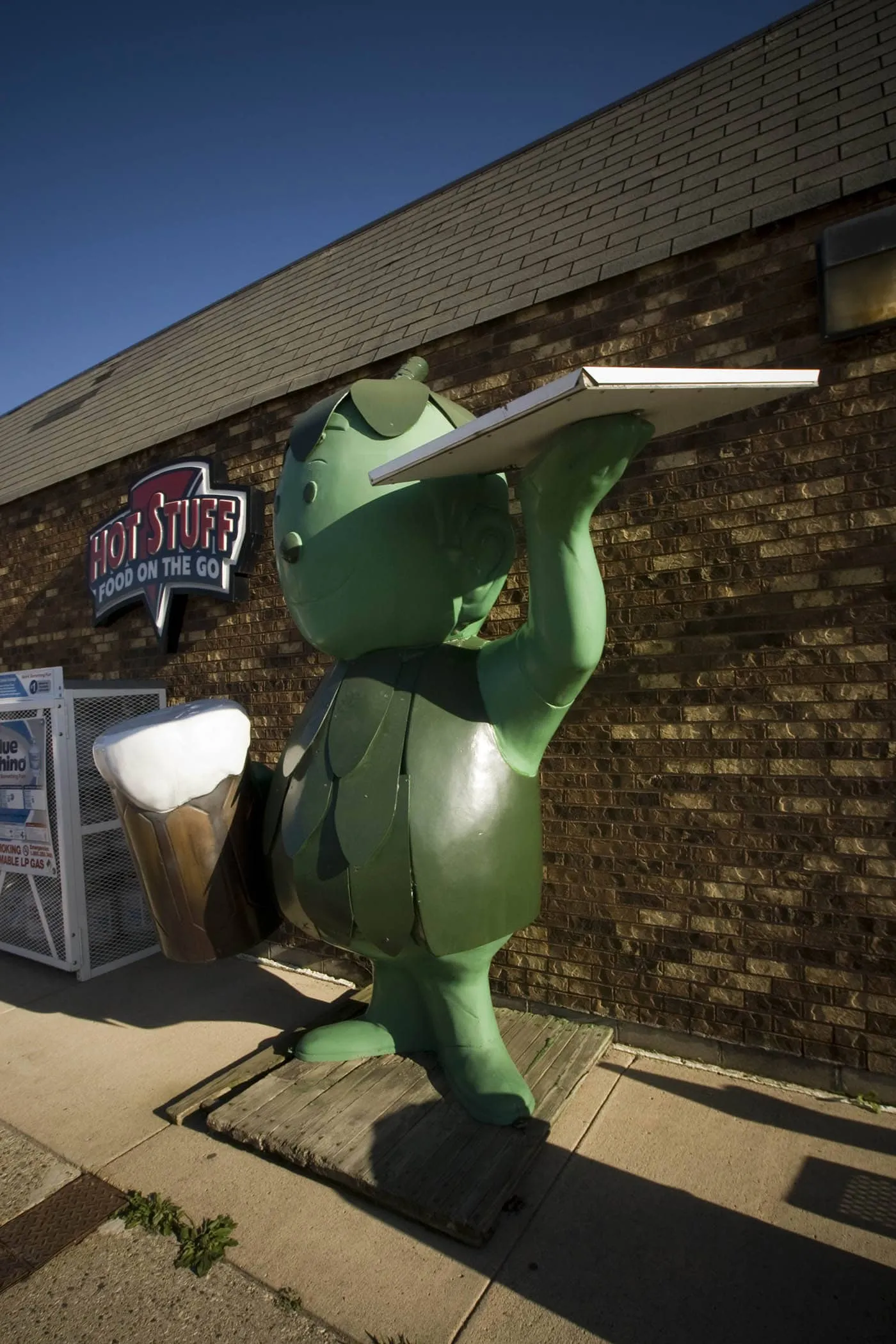 Fiberglass Little Green Sprout statue holds a beer and a pizza box outside of a gas station in Blue Earth, Minnesota.