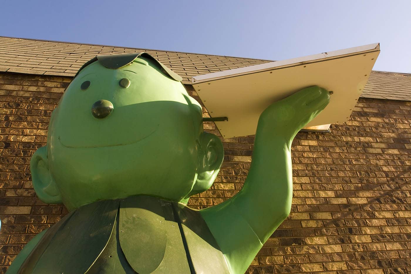 Fiberglass Little Green Sprout statue holds a beer and a pizza box outside of a gas station in Blue Earth, Minnesota.