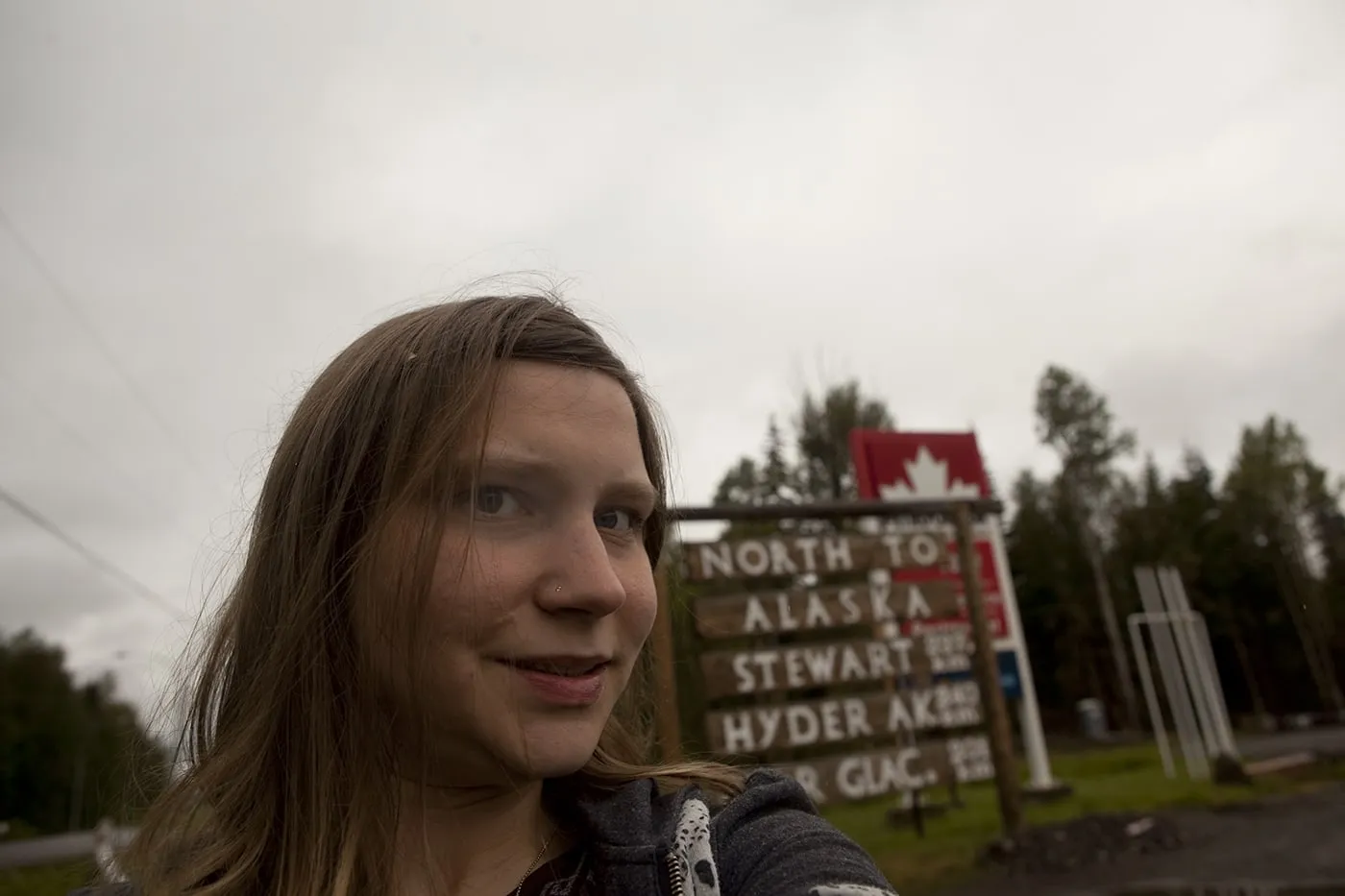 Val with the North to Alaska, Stewart, Hyder, Bear Glacier sign in Kitwanga,British Columbia, Canada.