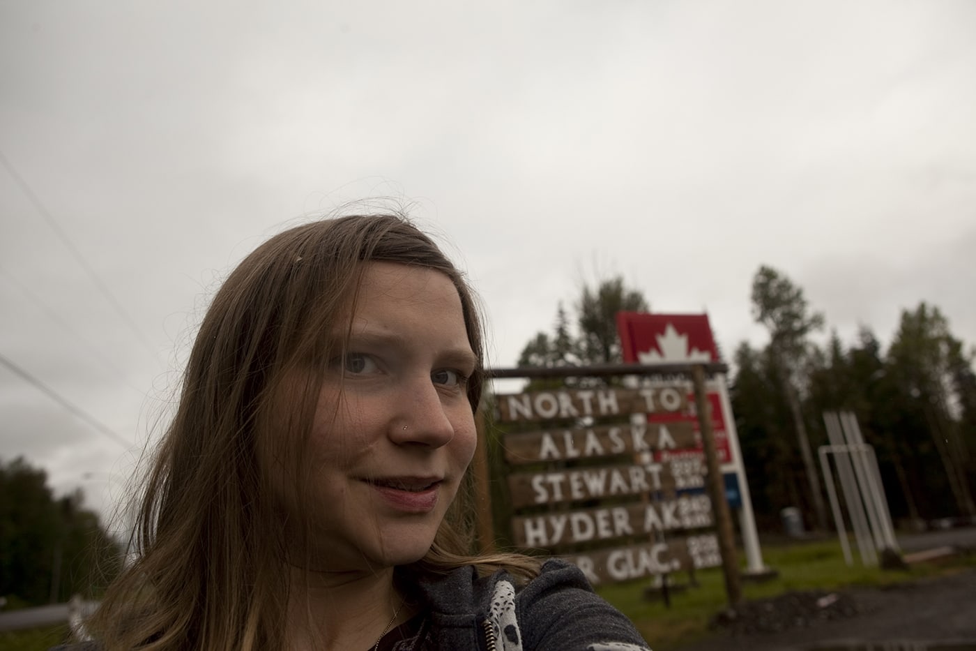 Val with the North to Alaska, Stewart, Hyder, Bear Glacier sign in Kitwanga,British Columbia, Canada.