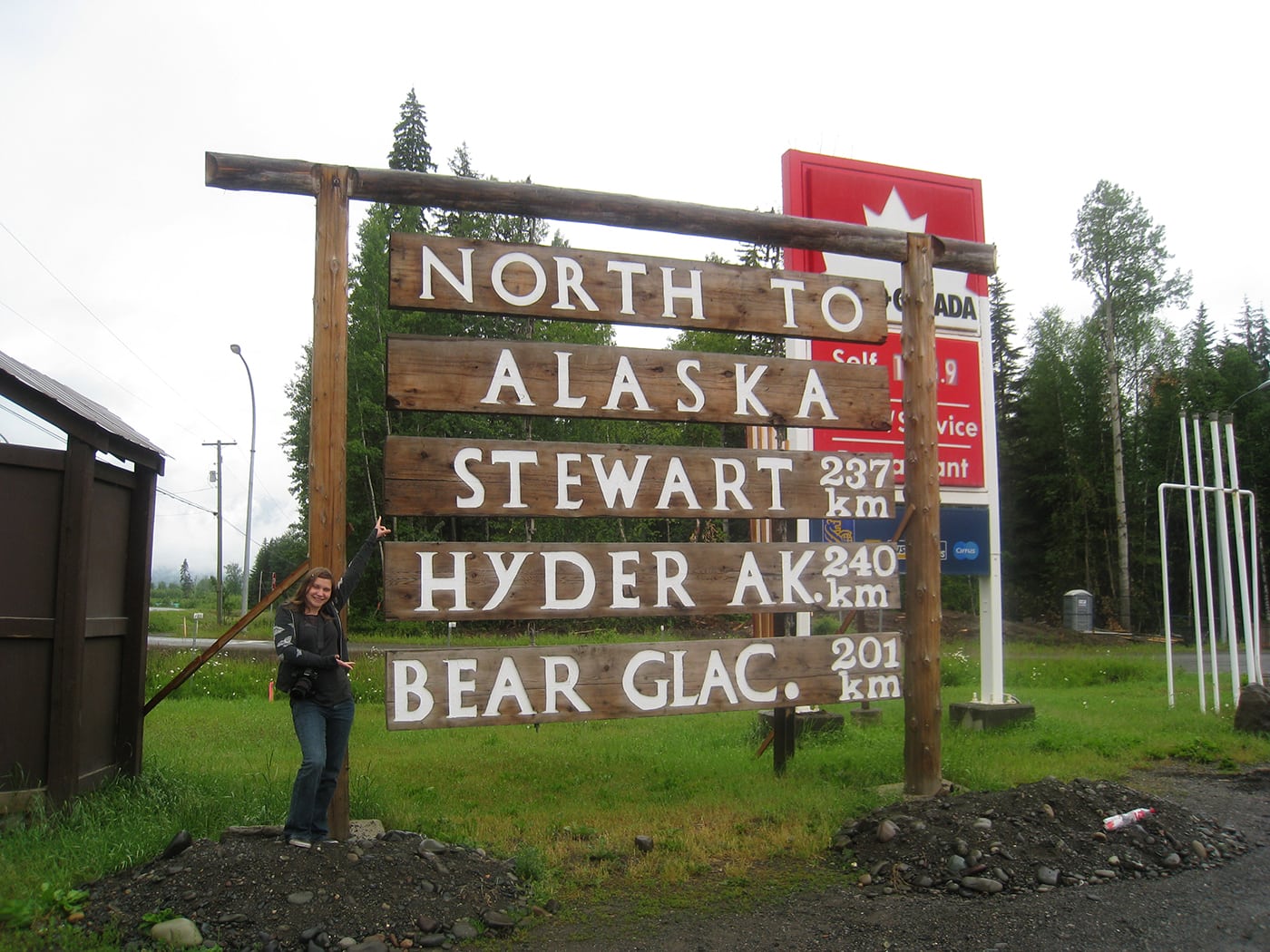 Val with the North to Alaska, Stewart, Hyder, Bear Glacier sign in Kitwanga,British Columbia, Canada.