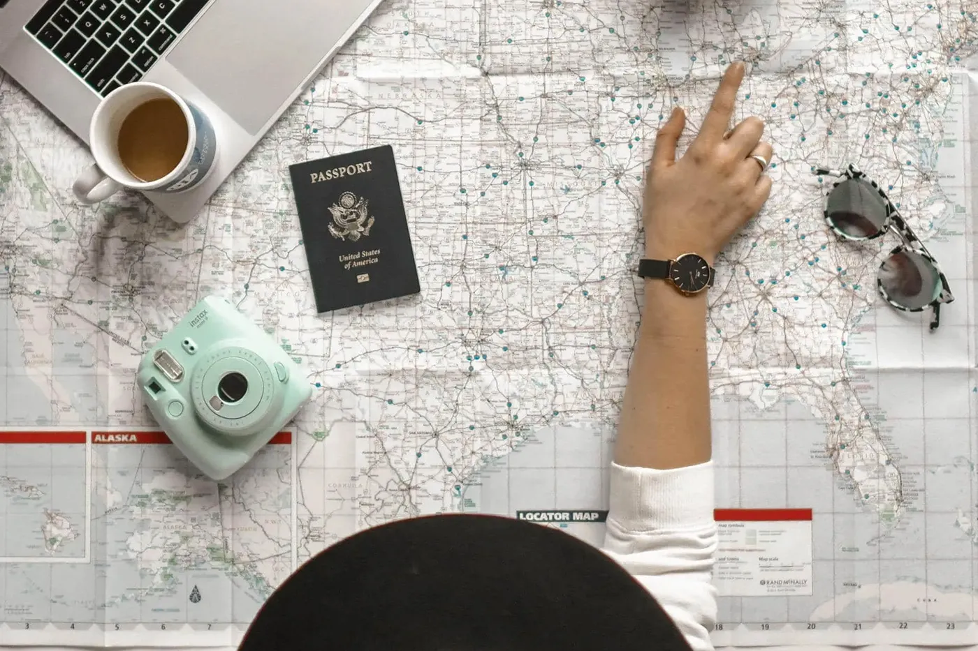 How to plan a road trip with Google Maps - woman pointing at a road map with a camera, passport, and laptop