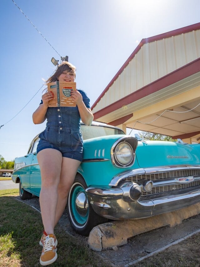 The Road Trip Journal & Activity Book - Reading a road trip book in front of a classic car at Desert Hills Motel on Route 66 in Tulsa, Oklahoma